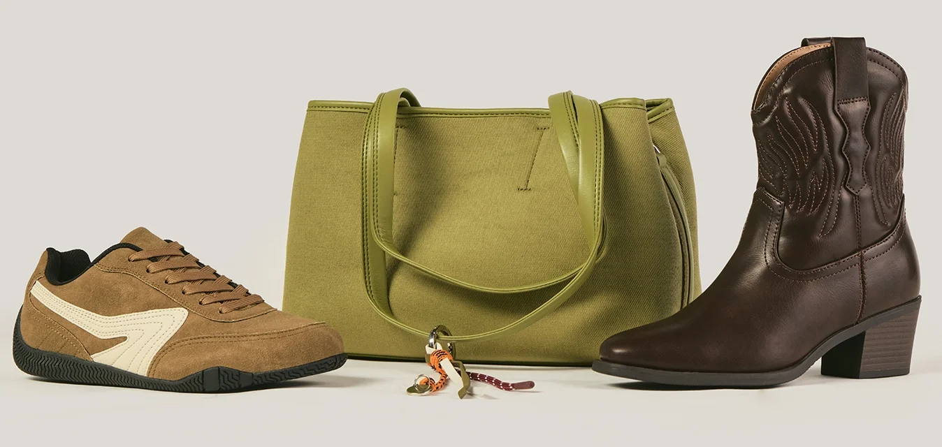 Sneaker in suede marrone, borsa in pelle verde oliva con portachiavi e stivaletto alla caviglia in pelle marrone scuro su sfondo neutro.
