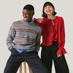 Uomo con maglione a righe seduto su uno sgabello, donna con camicetta rossa in piedi accanto a lui, sorridente e che indica in avanti.