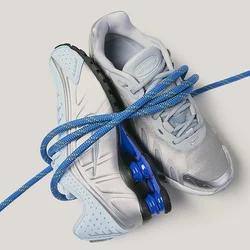Coppia di scarpe sportive grigio chiaro e blu intrecciate da una corda blu su uno sfondo chiaro.