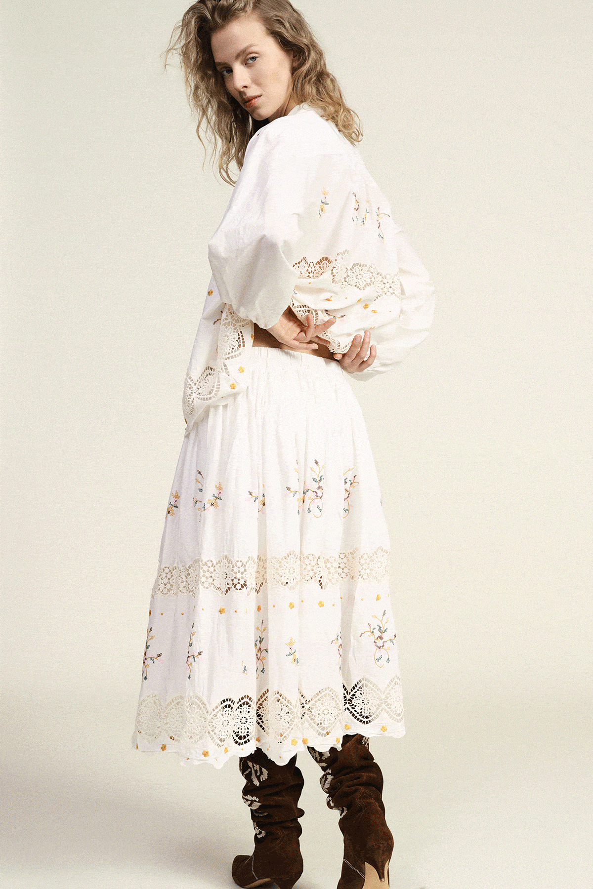 Two female models on a neutral background; close-up of mustard embroidered floral jacket and full-length white embroidered blouse with denim jeans