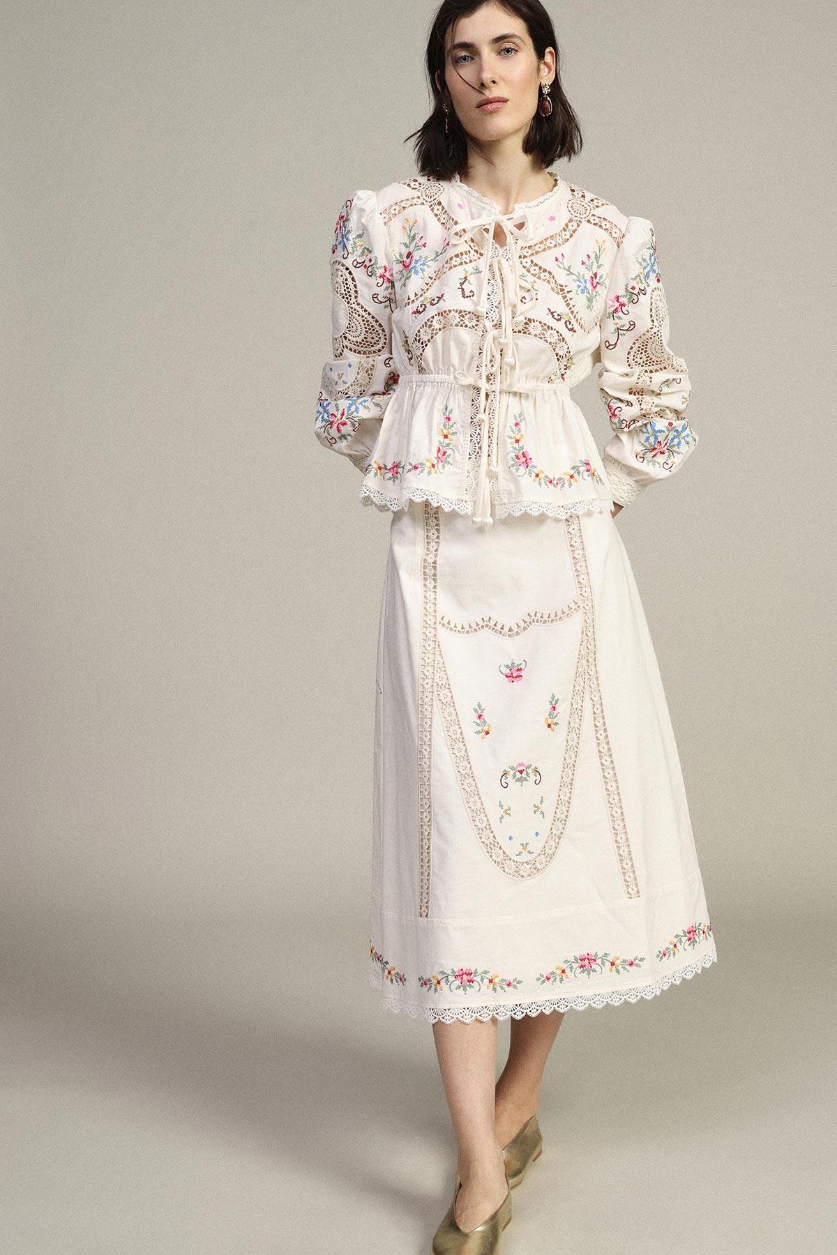 Model in cream embroidered boho blouse and matching midi skirt with floral embroidery and lace trim on neutral background