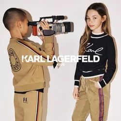 Completo in beige con dettagli a righe, maglione nero con scritta bianca e stivali militari neri. Scena di ripresa con una videocamera vintage.