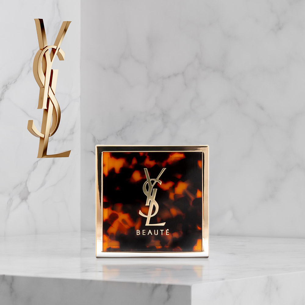 Uno specchio YSL Beaut&eacute; tartarugato su una superficie di marmo bianco.