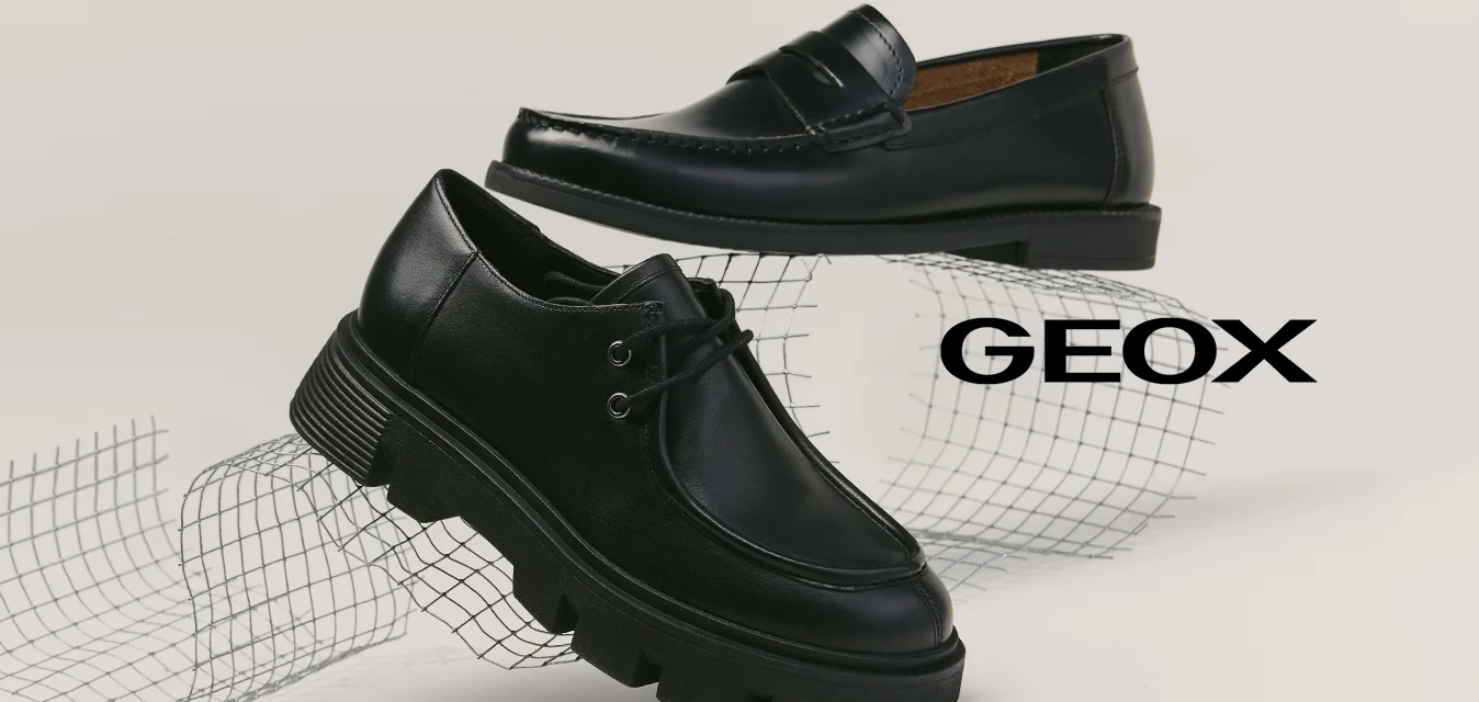 Due scarpe nere in pelle esposte su una superficie bianca, una mocassino con cuciture e una stringata con suola spessa, poggiate su una griglia di filo curva.