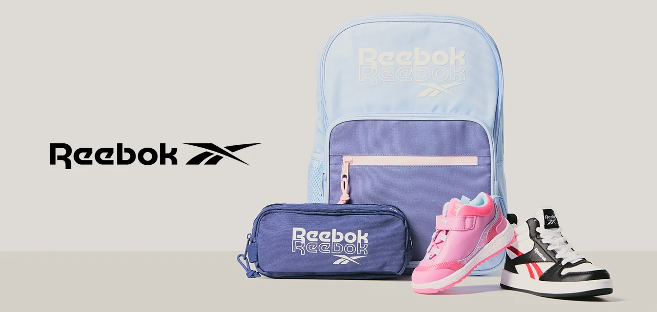 Zaino Reebok azzurro chiaro e viola, astuccio viola e due scarpe da bambino—una rosa, una bianca e nera—su sfondo grigio.