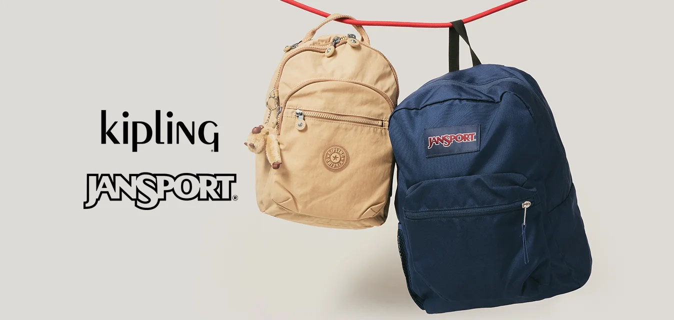 Zaini Kipling beige e JanSport blu che pendono per le cinghie da un cordone rosso su uno sfondo semplice.