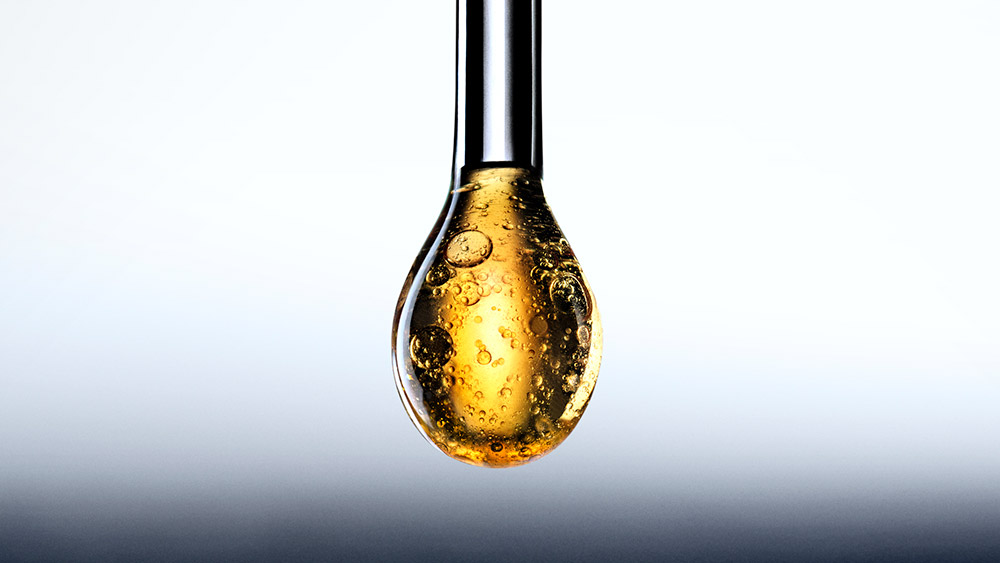 Goccia dorata e luminosa del siero Replasty sospesa al suo applicatore metallico, che rivela una texture concentrata con micro-bolle. 