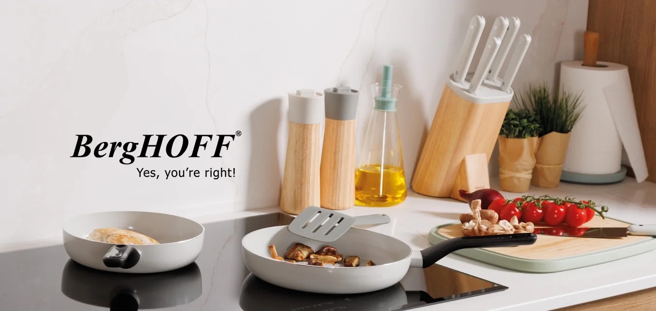 Due padelle su un piano cottura a induzione nero, armadietti in legno chiaro, schienale in marmo bianco e utensili da cucina tra cui un coltello, bottiglie e pomodori.