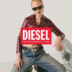 Persona in ginocchio sul pavimento che indossa occhiali da sole, una giacca di pelle color marrone scuro e jeans, con una mano appoggiata su un ventilatore da pavimento color argento.