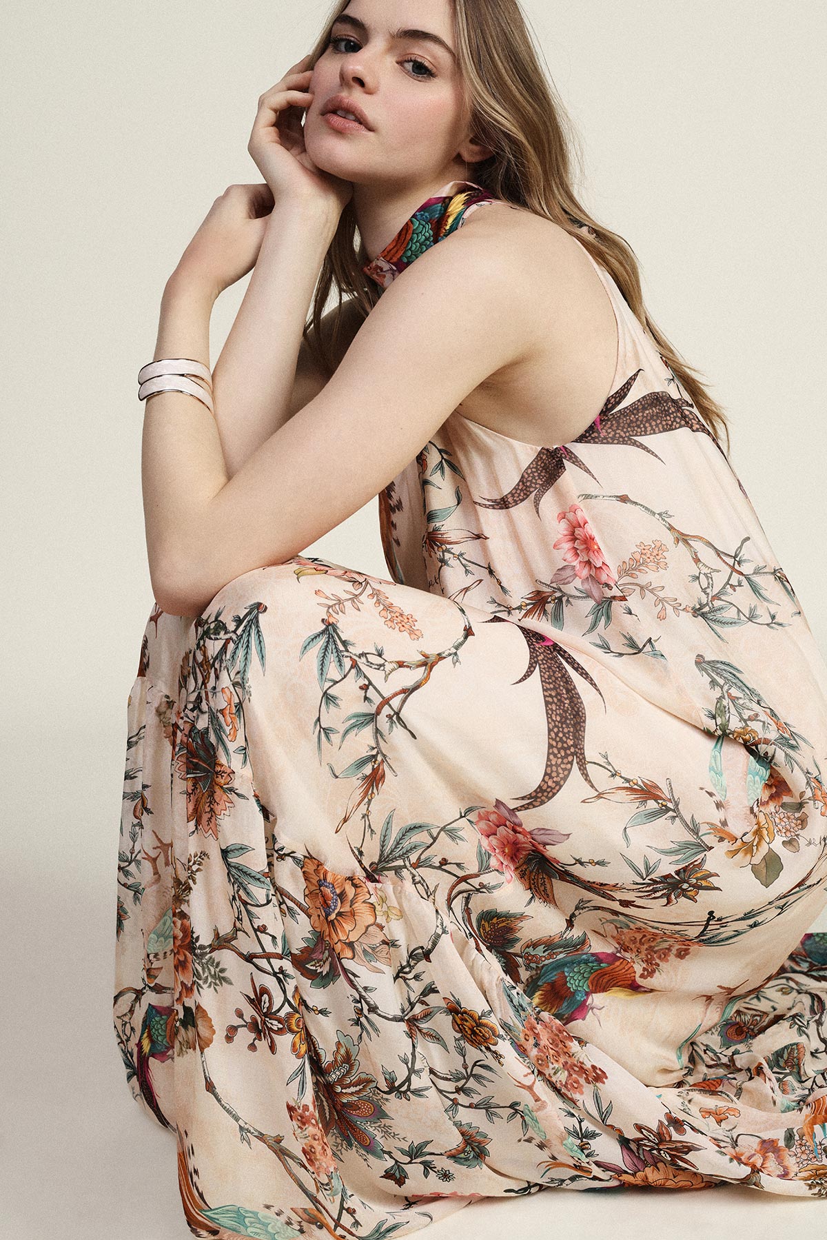 Woman modelling a sleeveless floral maxi dress in a crouched pose against a neutral background
