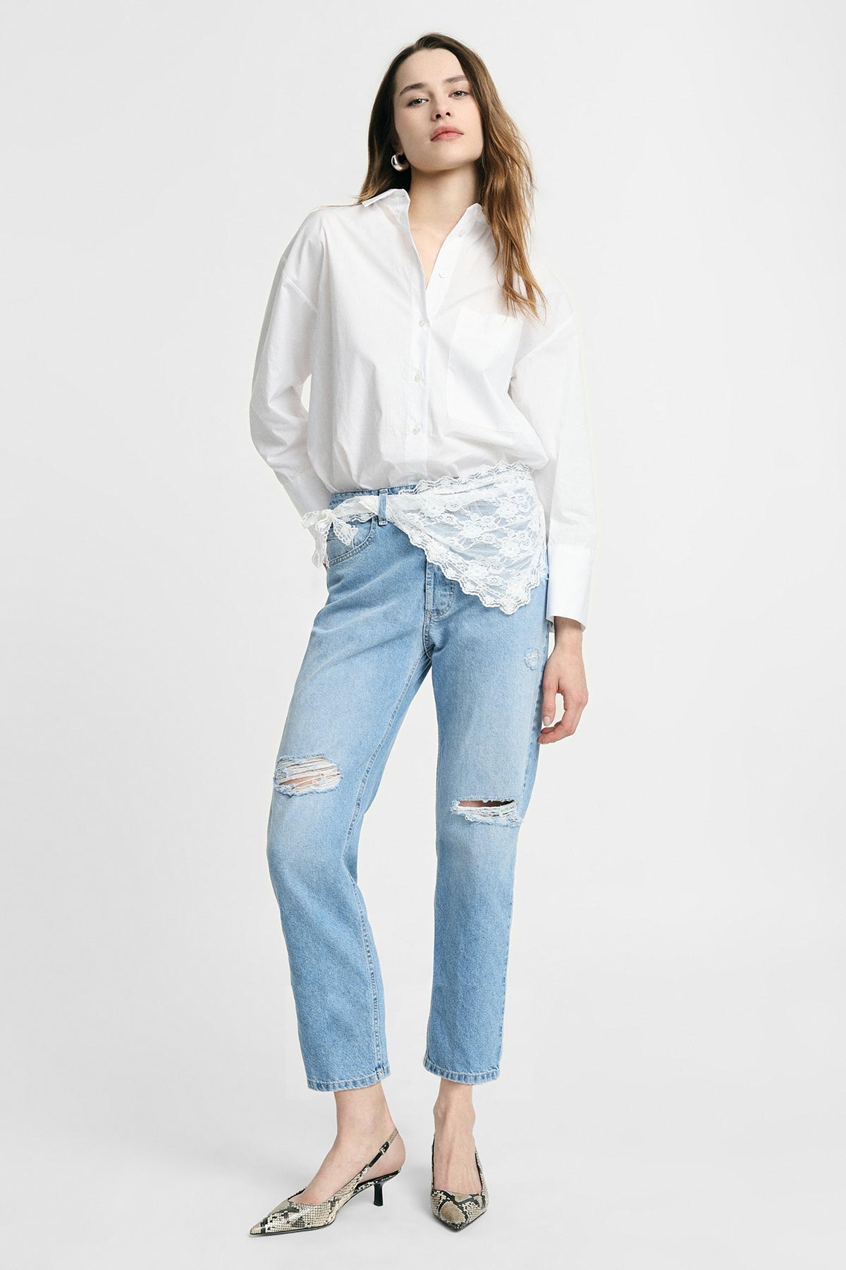 Full-length photo of woman modelling white button-down shirt with lace waist detail, ripped light-blue jeans and snakeskin heels