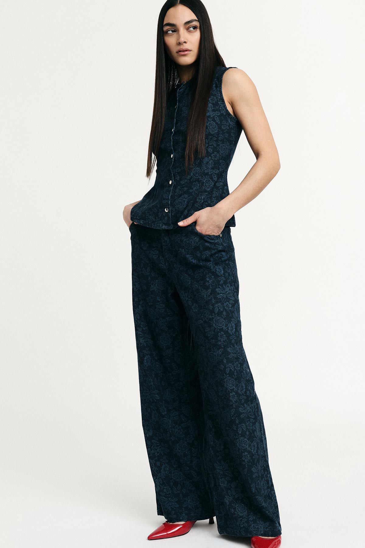 Woman modelling dark blue patterned sleeveless vest and matching wide-leg trousers with red pointed heels on plain background