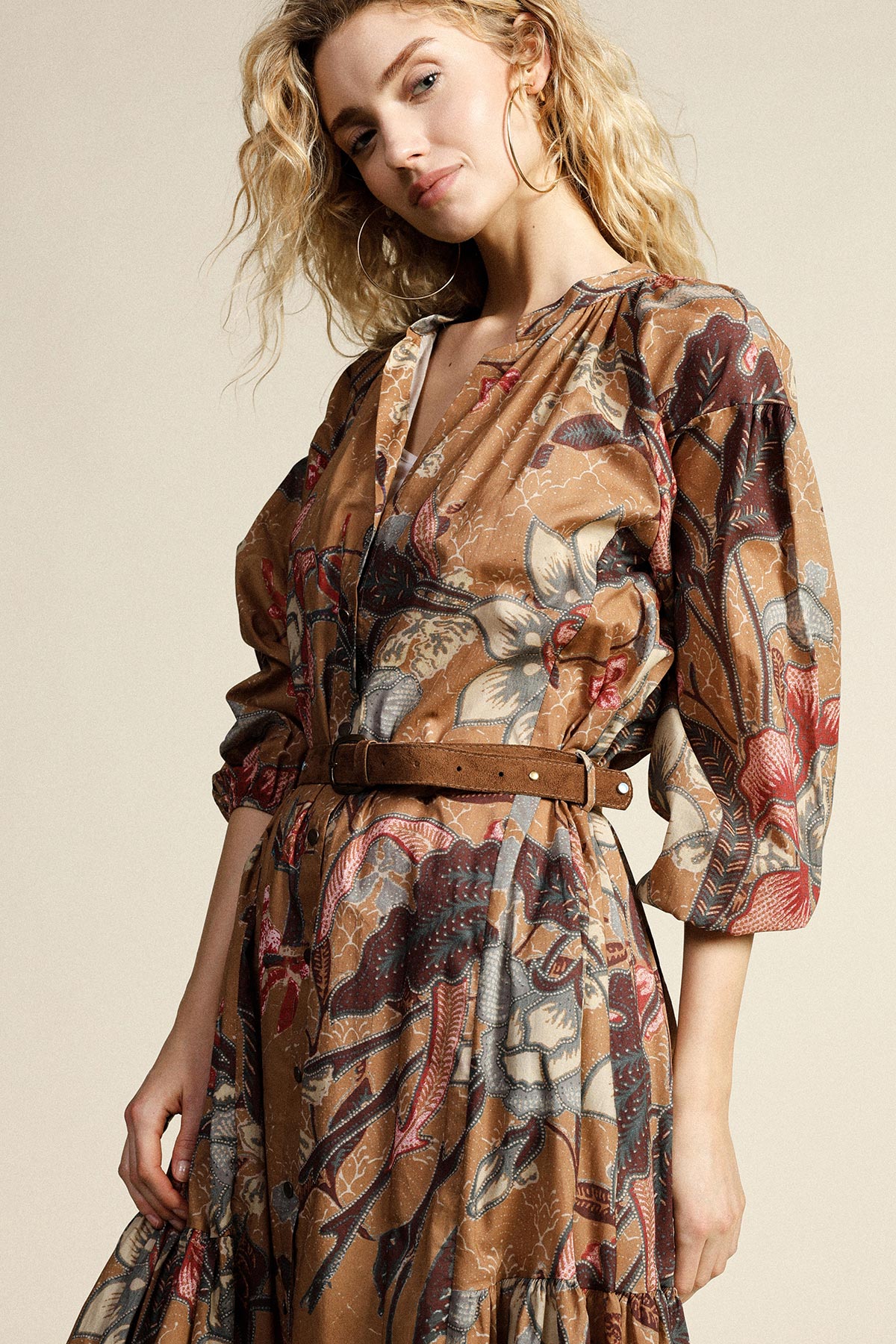 Woman wearing brown floral midi dress with puff sleeves and suede belt, posing against plain background