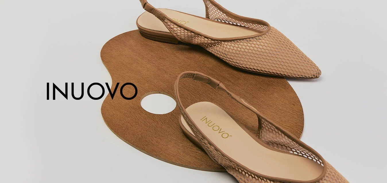 Scarpe piatte beige intrecciate con cinturino sul tallone e punte appuntite, posate su una tavolozza da artista marrone su uno sfondo bianco.