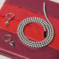 Portafoglio bordeaux piegato con una striscia rossa, accompagnato da una collana d'argento con perline, due orecchini a cerchio d'argento con ciondoli e un braccialetto a catena.