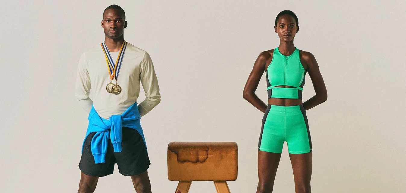 Due atleti si trovano ai lati opposti di un cavallo da pommel; l'uomo indossa medaglie e abbigliamento sportivo, mentre la donna indossa un completo atletico verde.