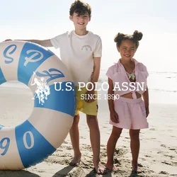 Due bambini in piedi a piedi nudi su una spiaggia sabbiosa, uno tiene un grande anello gonfiabile da nuoto blu e bianco con la scritta 