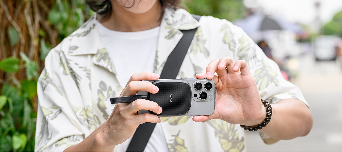 Una persona che scatta una foto su un telefono cellulare con un SSD SanDisk Phone fissato magneticamente sul retro del telefono.