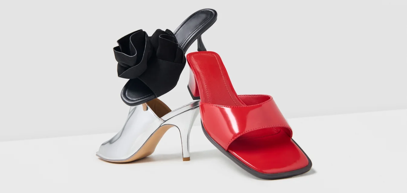 Mule rosso aperto davanti e scarpa con tacco alto argento con dettagli floreali neri, posizionati affiancati su una superficie bianca.