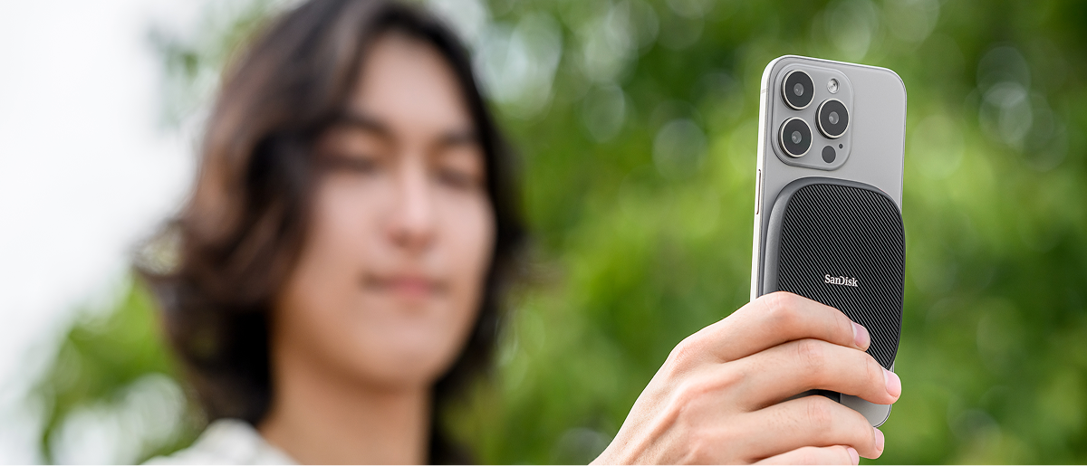 Una persona che tiene in mano un telefono cellulare con un SanDisk Phone SSD fissato magneticamente sul retro del telefono