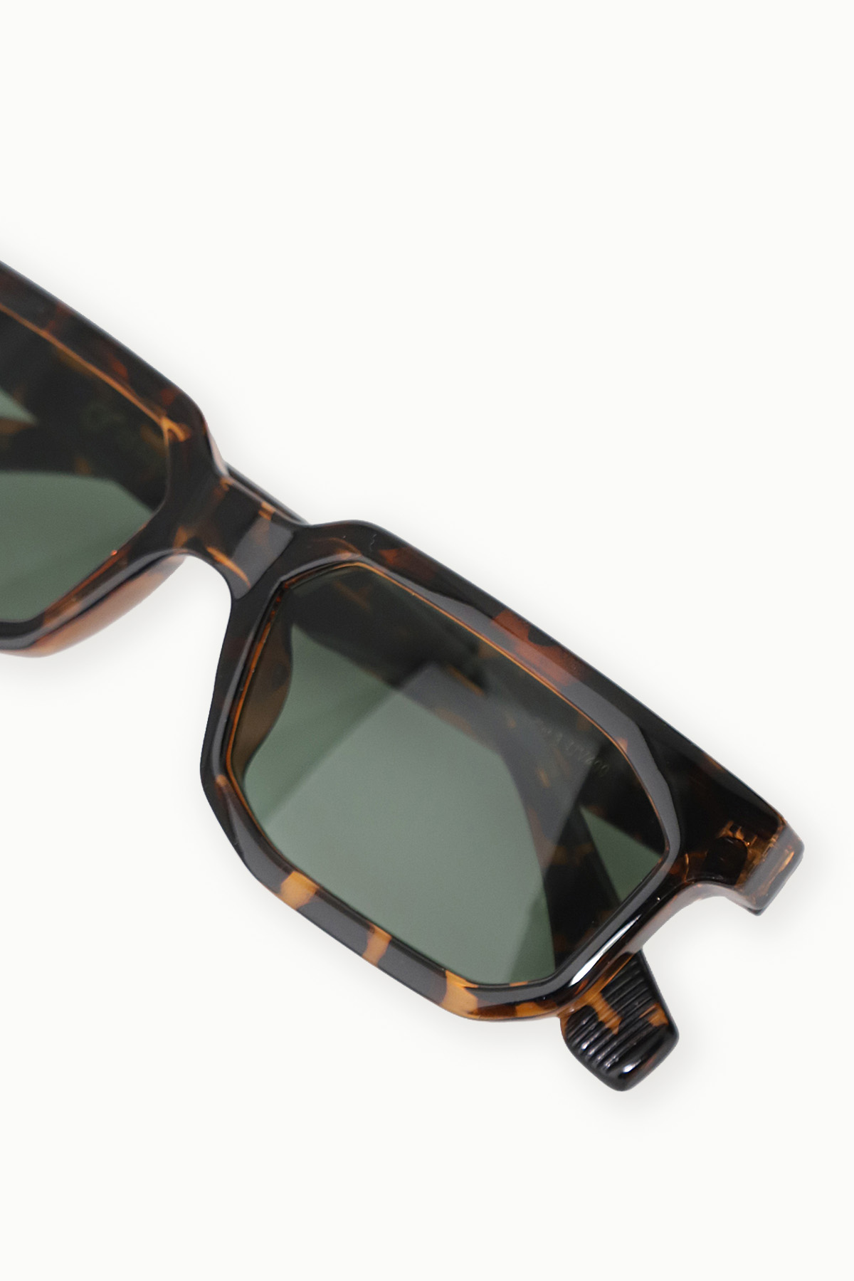 Close-up of tortoiseshell rectangular sunglasses with green lenses on a white background