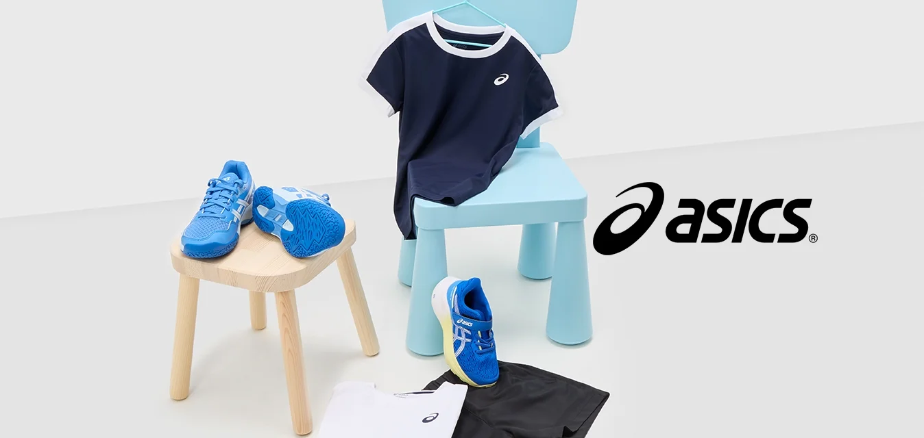 Scarpe sportive blu con accenti bianchi, t-shirt blu navy con bordi bianchi, pantaloni corti neri e camicia bianca su superfici chiare con una sedia blu.
