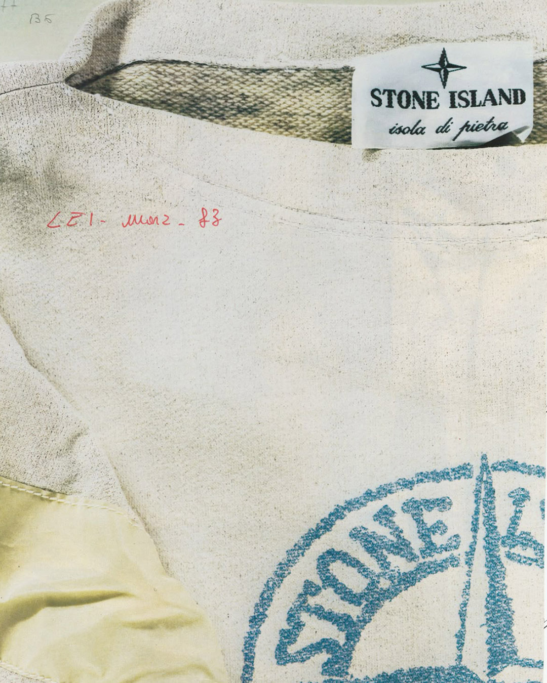 Close-up of Stone Island clothing label and stitched collar on a worn white t-shirt with a partial blue compass logo stamp