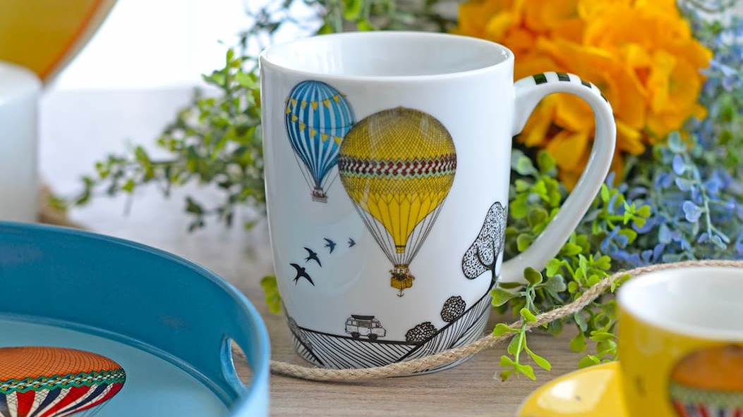 A mug with a character and a tray with hot air balloons on a wooden table.