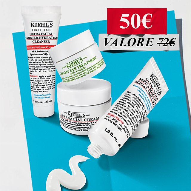 Composizione di prodotti Kiehl's in formato mini size: detergente, crema viso, contorno occhi all'avocado e crema corpo disposti su uno sfondo azzurro e bianco.