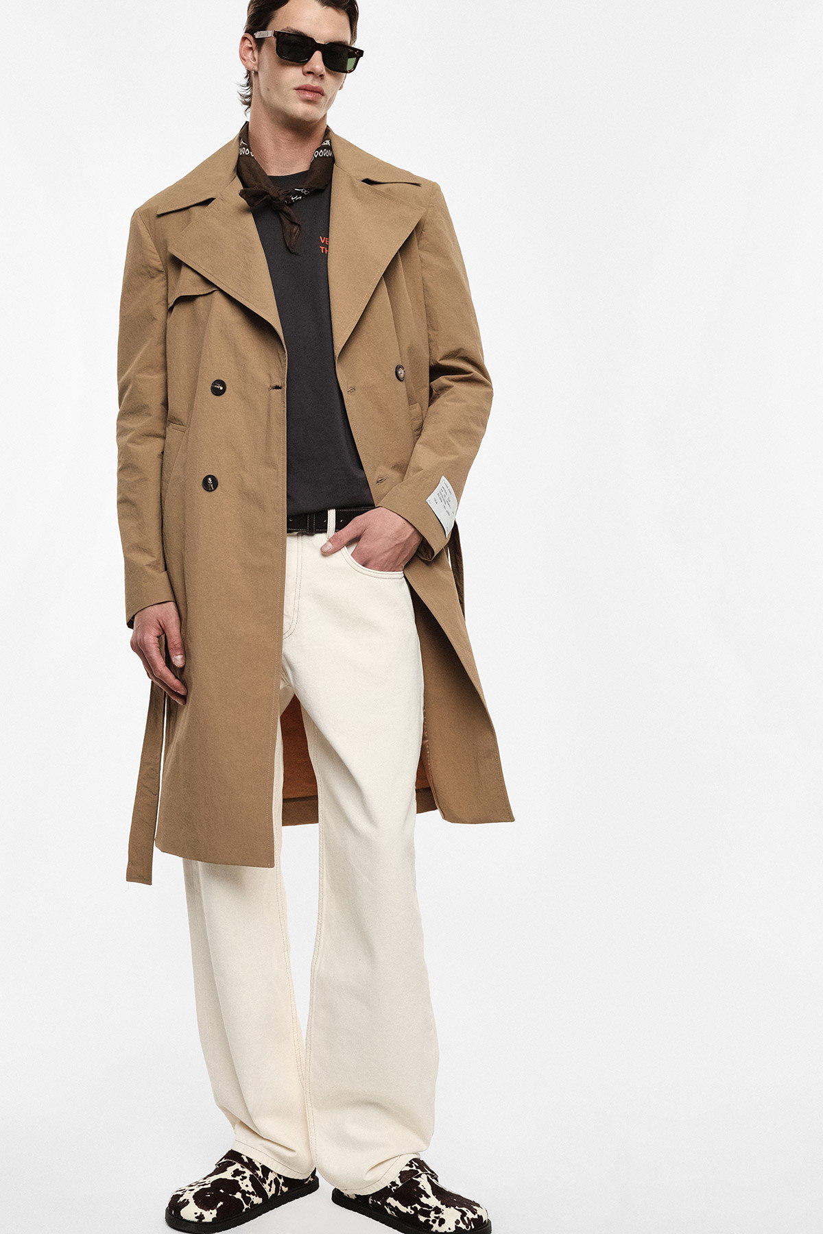 Model wearing camel trench coat, black T-shirt, cream wide-leg trousers, cow-print shoes and sunglasses