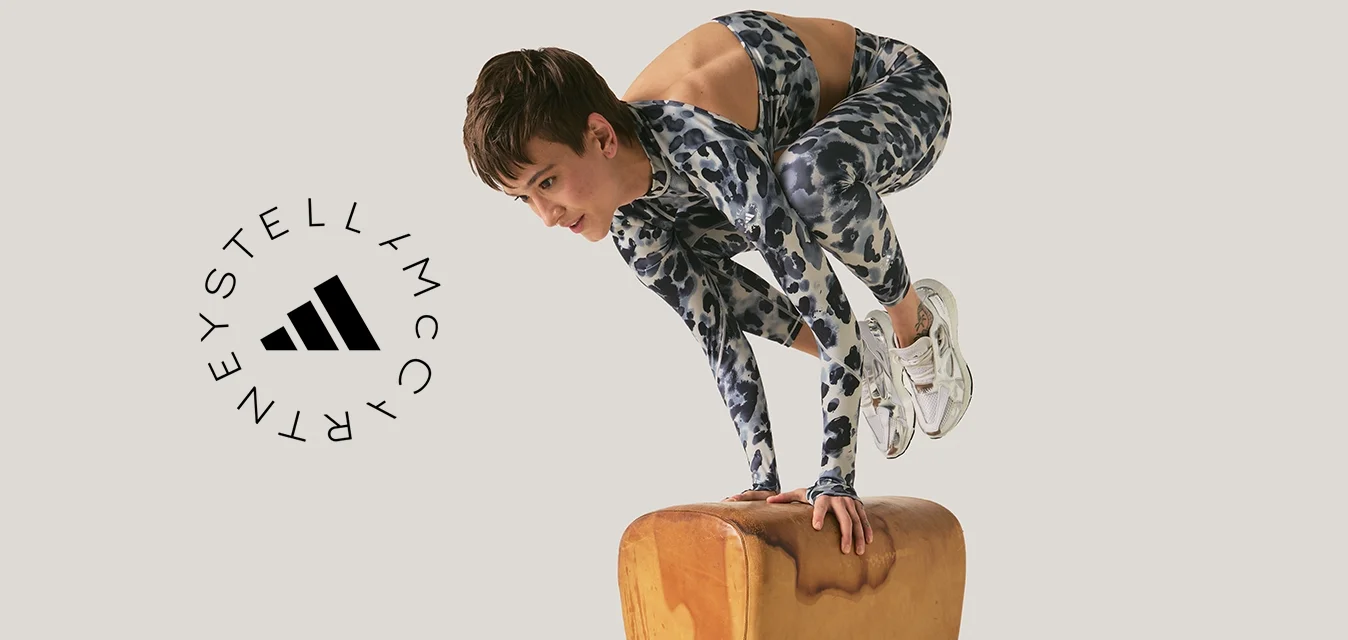 Persona in abbigliamento sportivo che si equilibra sulle mani sopra un cavallo con maniglie per ginnastica su uno sfondo semplice.