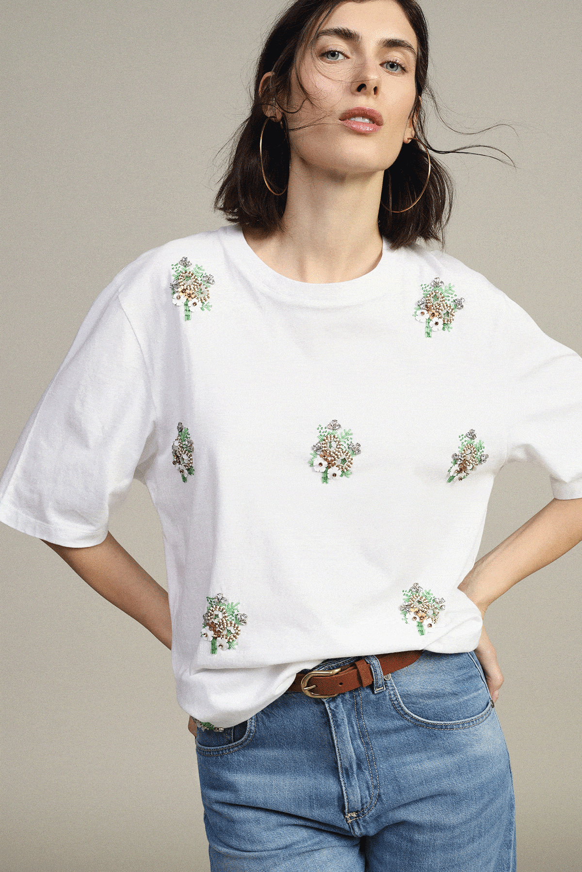 Two women modelling casual looks: white floral embroidered tee with jeans; grey wide‑leg sweatpants with sweatshirt tied at shoulders