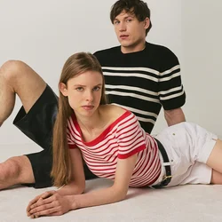 Giovane uomo e donna posano sul pavimento davanti a uno sfondo neutro, indossando magliette a righe, pantaloncini e stivali neri.