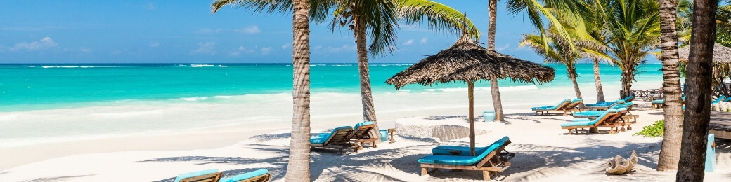 Tropical white-sand beach with palm trees, thatched umbrellas and turquoise sea; wooden sunloungers with blue cushions
