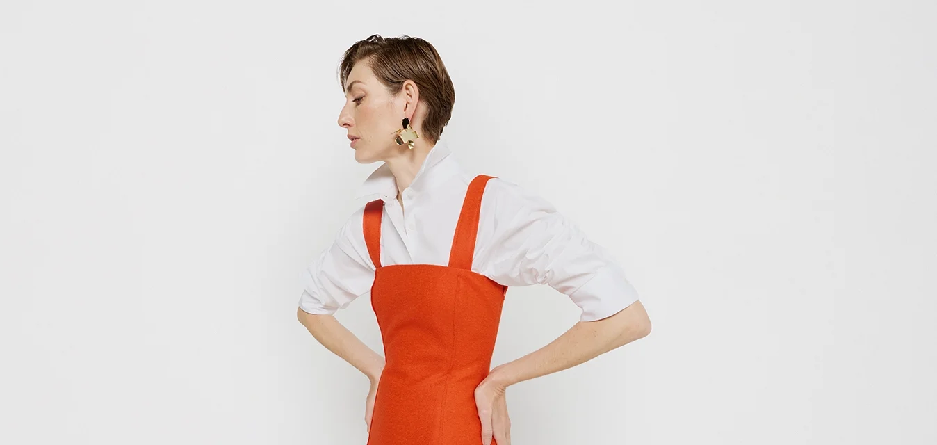 Abito rosso senza maniche con corpino aderente e gonna svasata, abbinato a una camicia bianca con bottoni. Tessuto liscio, design minimalista.