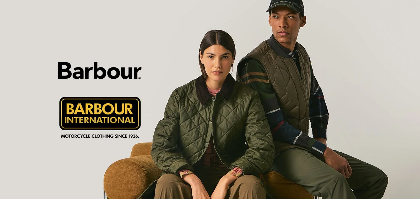 Due persone con abbigliamento outdoor verde siedono e si appoggiano a un cuscino rotondo marrone su uno sfondo beige uniforme.