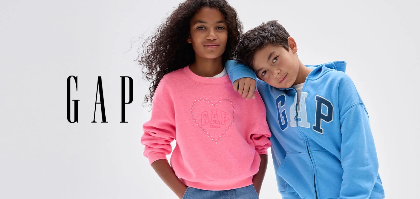 Due bambini stanno insieme; la ragazza con felpa rosa e jeans larghi, il ragazzo con felpa blu GAP e jeans appoggia la testa sulla spalla della ragazza.