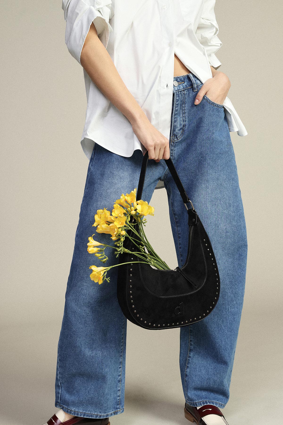 Person in white shirt and wide-leg blue jeans holding a black crescent handbag filled with yellow flowers