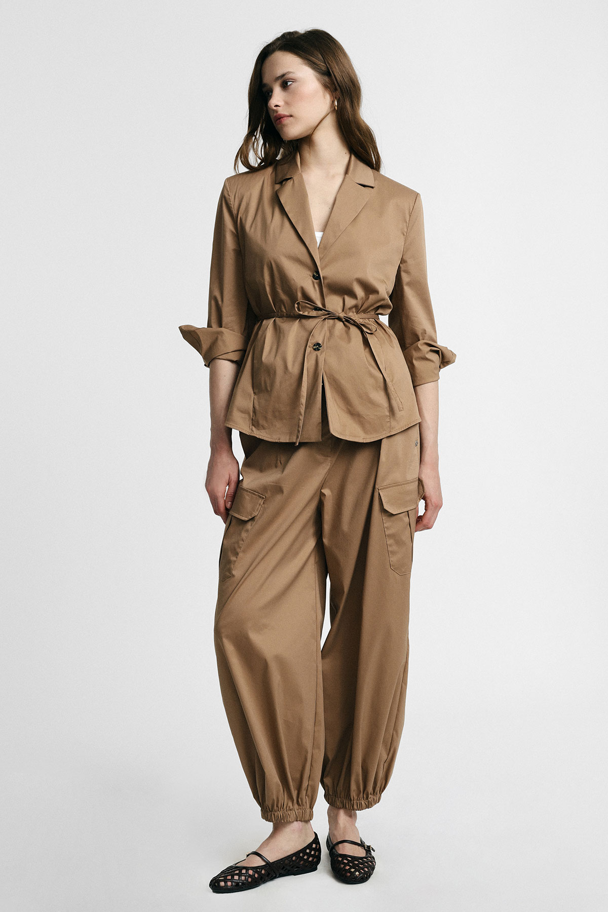 Woman modelling tan utility jacket with tied waist and matching cargo trousers with elasticated cuffs, wearing black woven flats on white background