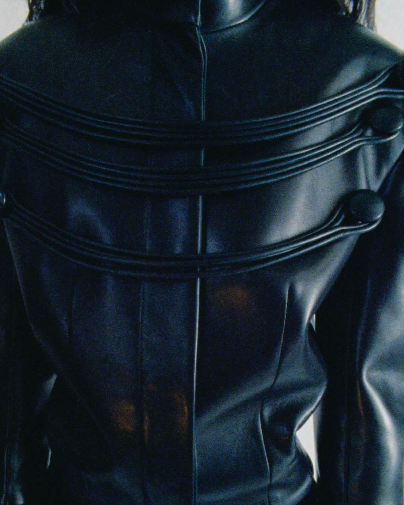 Close-up of glossy black leather jacket back with three horizontal padded piping bands and round button details