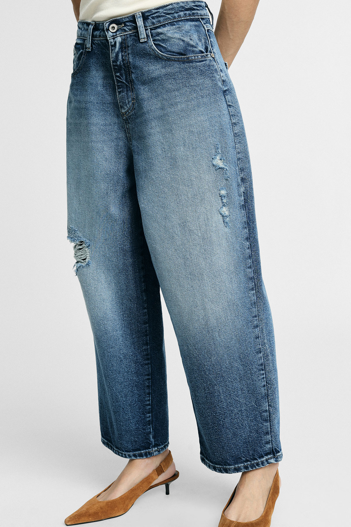 Cropped view of model wearing wide-leg distressed blue jeans paired with brown suede kitten-heel slingback shoes