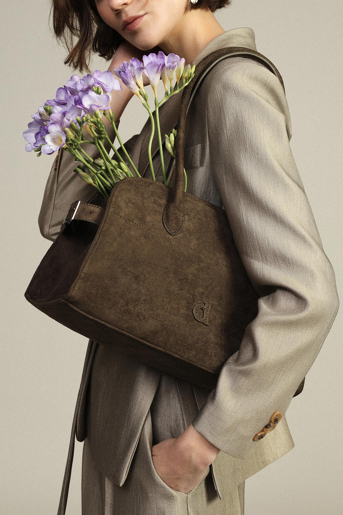 Woman in beige blazer holding a brown suede handbag filled with purple freesia flowers