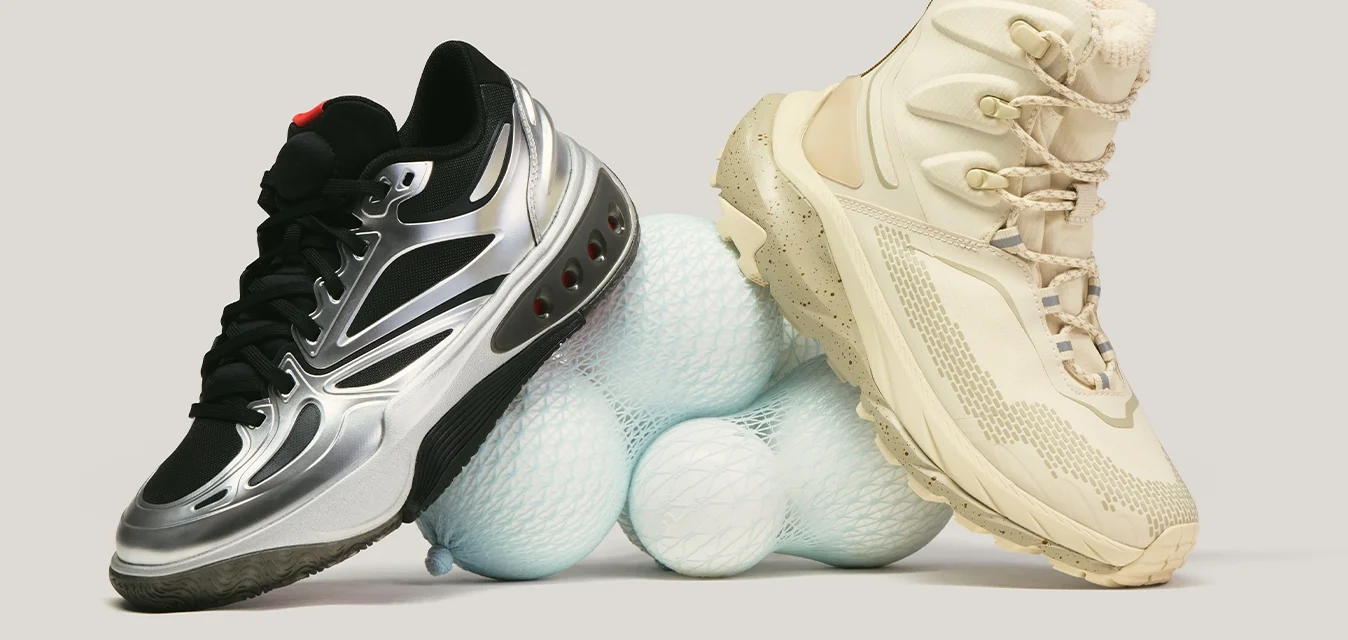 Scarpa sportiva nera e argento e scarponcino da trekking beige poggiati su una pila di palline da golf bianche su uno sfondo chiaro.