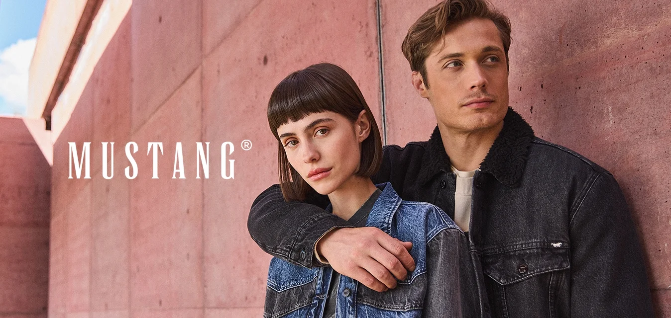 Due modelle sono in piedi contro un muro di cemento rosa, indossando giacche di jeans. Una giacca presenta uno yoke blu, mentre l'altra è scura con un colletto testurizzato.