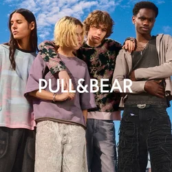 Cinque giovani adulti che indossano abiti larghi e casual e pantaloni corti si trovano vicini l'uno all'altro davanti a uno skyline cittadino sotto un cielo blu.