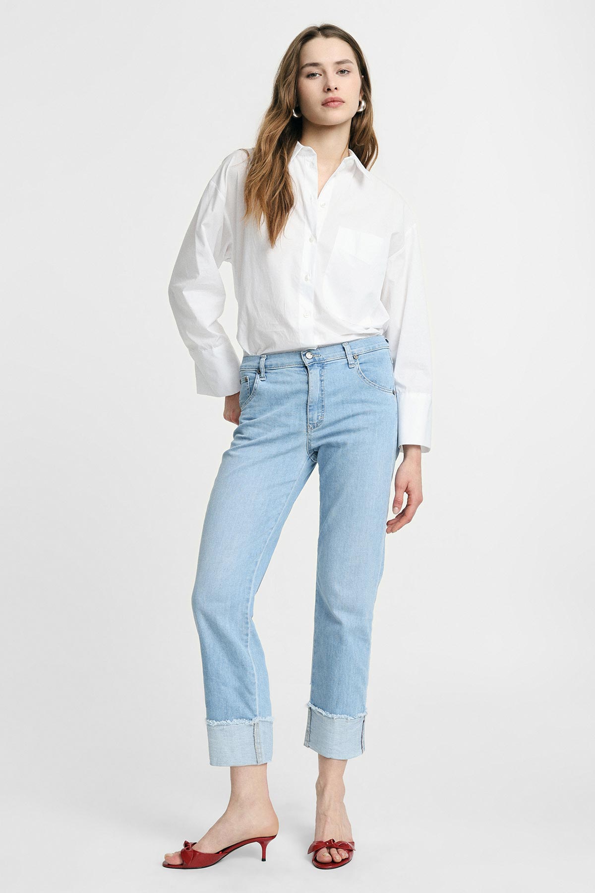 Model wearing white oversized button-up shirt, light blue cuffed jeans and red low-heel mules on white background