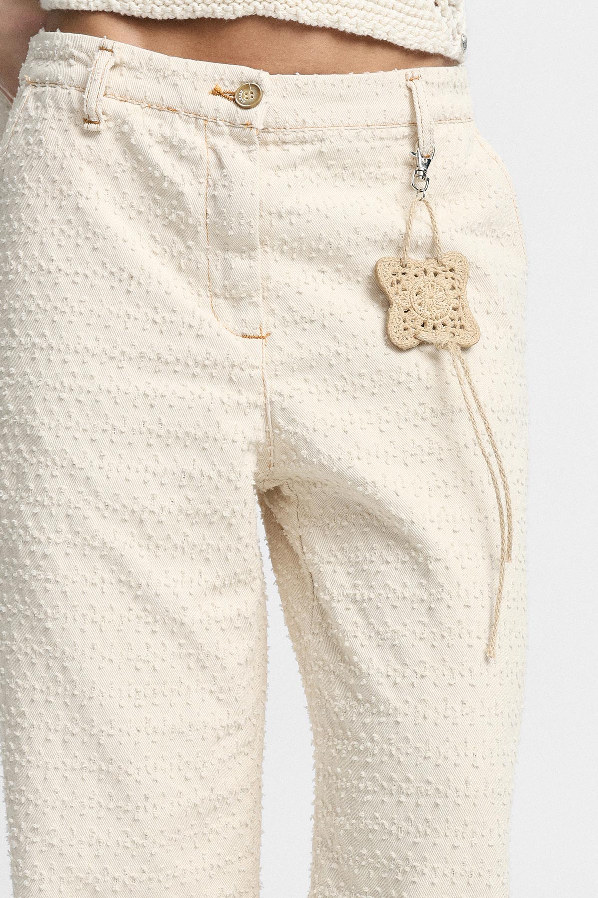 Cream textured high‑waist trousers close-up with crocheted star keyring clipped to belt loop, matching cropped top visible