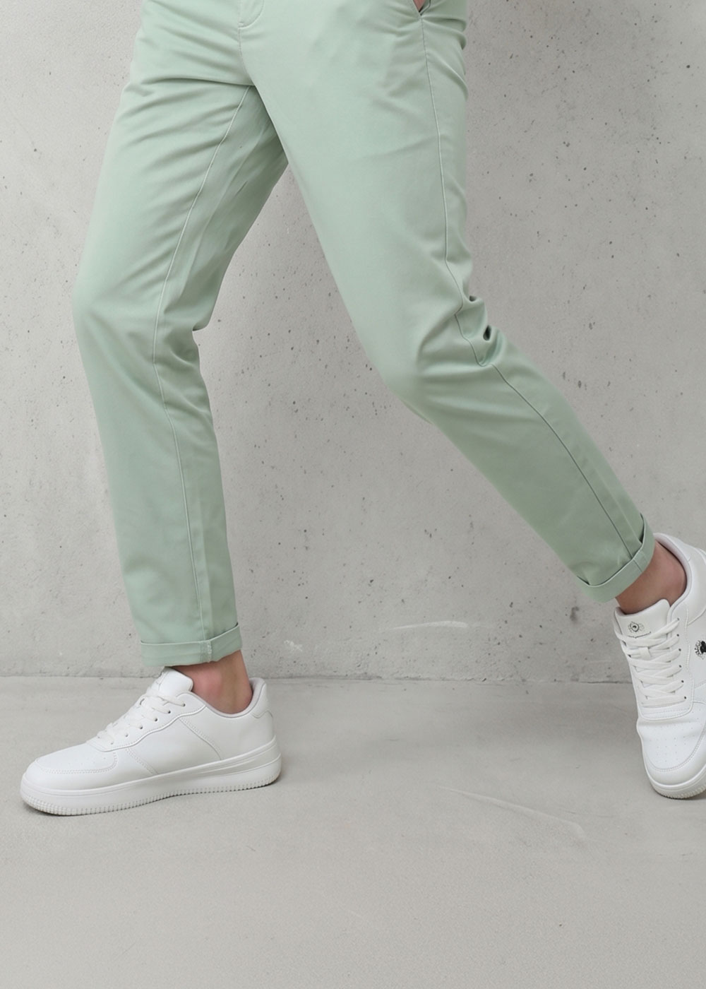 Person wearing mint-green slim-fit trousers with cropped hem and white sneakers standing on a concrete floor