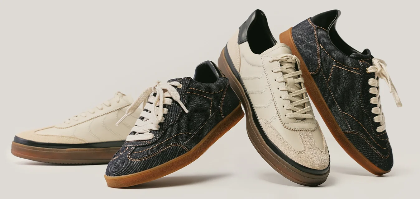 Coppia di sneakers casual, una beige con suola marrone, l'altra in denim scuro con lacci beige, disposte in piedi su uno sfondo neutro chiaro.