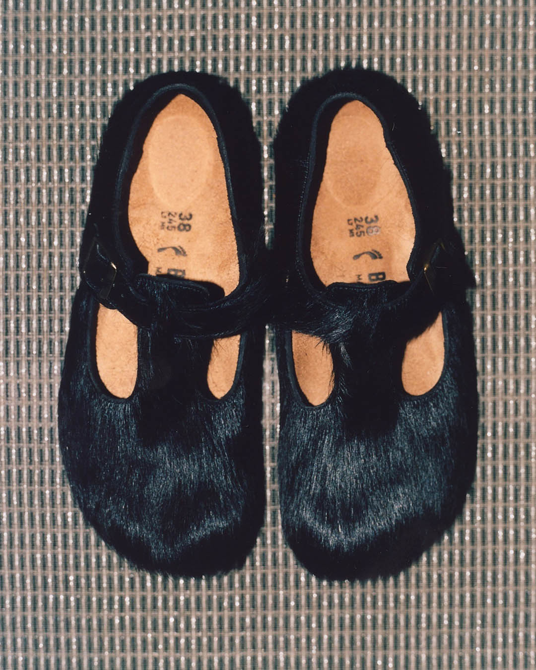 Pair of black faux-fur Mary Jane shoes with buckle straps, size 38 visible inside, on a woven mat background